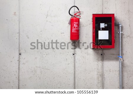 A fire extinguisher and a fire-hose on concrete wall