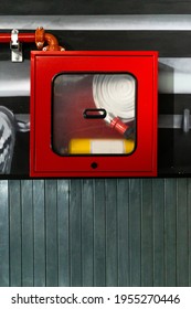 A Fire Extinguisher And Its Hose Stored In A Red Glass Box In The Emergency Area, Under A Wooden Wall