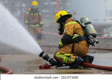 A fire fighter is controlling a fire monitor in order to combat fire. Visible water mist in the background.