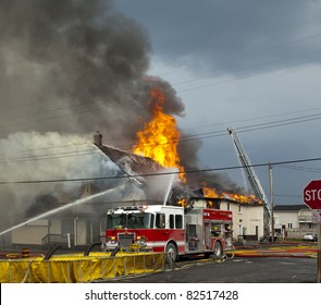 Fire Fighters Responding To Fire In A Large Building Engulfed In Flames