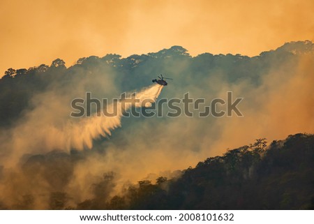 Fire fighting helicopter dropping water on forest fire