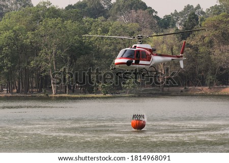 Fire Fighting and Rescue Helicopter with Bambi Bucket are Carrying Water from Reservoir to put out a Forest Fire.