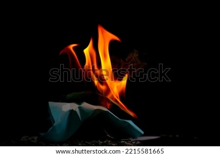 Fire flame burning paper on black background, flame glowing of fire on dark wallpaper, close up fire tongue show energy, ash from burning paper on ground, red and yellow flame fire for creative photo
