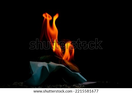 Fire flame burning paper on black background, flame glowing of fire on dark wallpaper, close up fire tongue show energy, ash from burning paper on ground, red and yellow flame fire for creative photo