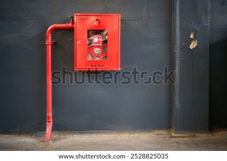 Fire hose in red box. Pipe roll for fire emergency in red metal cabinet on gray painted concrete wall with tiled floor as part of firefighting system of industrial production plant with copyspace.