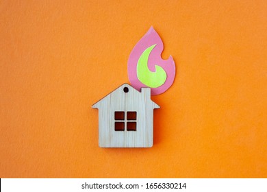 Fire House, Insurance And Mortgage Concept. Small Wooden House Toy And Paper Fire Shape On Orange Background Top View