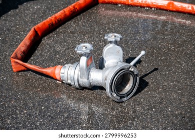 Fire hydrant adapter with connected pressure hose used to supply water to a portable fire pump during firefighting operations. Close-up of firefighting equipment and water supply infrastructure during a training exercise or emergency response.