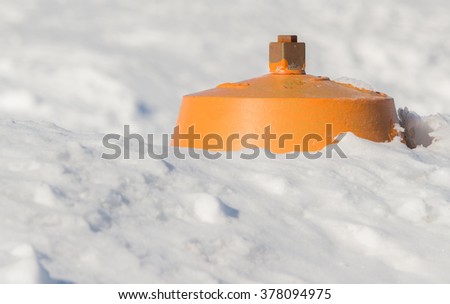 A fire hydrant almost completely buried in a snowbank. The top is yellow, the rest is not visible. The foreground and background is snow. Focus is on the square valve stem on top. Room for text.