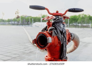 Fire hydrant connected to a hose on a rainy pavement, with water flowing around the base in a city environment.