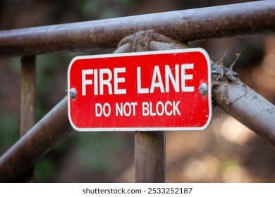 Fire Lane Do Not Block red metal sign on a gate in a local park, blurred trees in the background, no people, daylight