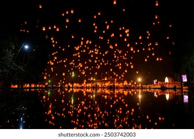 Fire Lanterns Floating up into the sky is reflection in the water at night at Loi Krathong Festival Travel Destinations Of Chiang Mai, Thailand. Sky fire lantern at night in the Yee Peng Festival