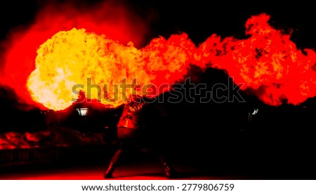Fire performer uses a torch to create bright flames at night during an outdoor event with people gathered in urban surroundings