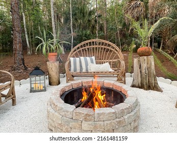 Fire pit bonfire campsite in tropical backyard woods with rustic wooden branch chairs twinkle lights lantern candles palm trees stump tables in Florida at sunset - Shutterstock ID 2161481159