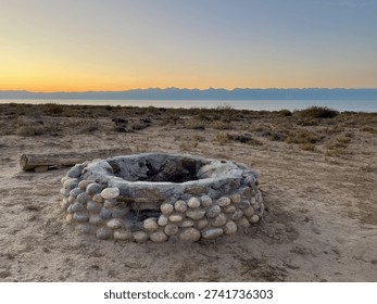 Fire pit on a sandy beach at Lake Issyk-Kul, with Tian Shan mountains in the background at sunset, Kyrgyzstan.