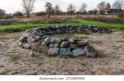 Fire pit ring constructed from large natural granite and fieldstone boulders placed on sandy ground in an open grassy park area. Outdoor campsite feature designed for campfire gatherings and recreation.
