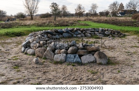 Fire pit ring constructed from large natural granite and fieldstone boulders placed on sandy ground in an open grassy park area. Outdoor campsite feature designed for campfire gatherings and recreation.