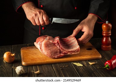 For A Fire, Raw Ribs Must Be Cut Into Small Pieces. Hands Of A Chef With A Knife In The Kitchen. Cooking Delicious Food For A Restaurant