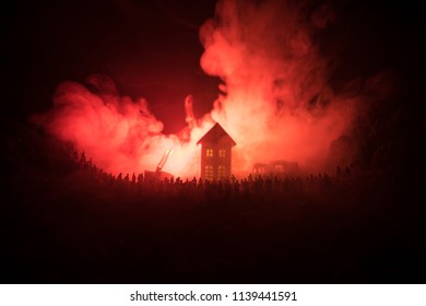 Fire Safety Concept. Huge Flame Distracting House On Fire. Fire Engine With Ladder And Fireman Trying To Save House. Fireman At Work. Silhouettes Of A Large Crowd Of People Watching At Fire At Night.