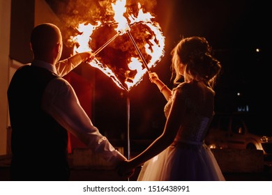 Fire show at the wedding. The bride and groom on the background of a fiery heart and fireworks and fireworks