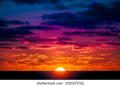Fire Sky. Ship silhouetted against a deep orange sunset over the ocean. The setting sun illuminates clouds with a rainbow of colors.
