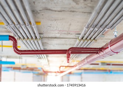 Fire Sprinkler System With Red Pipes Is Placed To Hanging From The Ceiling Inside Of An Unfinished New Building.Installation Of Conduits In Buildings.Conduit System In Building Under Construction.