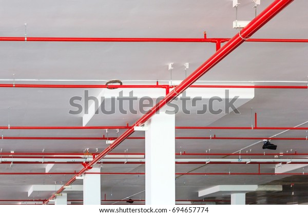 Fire\
sprinkler system with red pipes is placed to hanging from the\
ceiling inside of an unfinished new\
building.