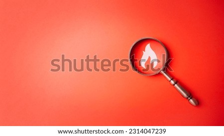 Fire surveillance inspection indicator and fire fighting with magnifying glass on red orange background. Fireman and conflagration concept. Wildfire and forest fire theme.