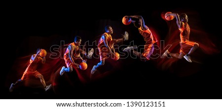 Fire tail or ways. African-american young basketball player of red team in action and neon lights over dark studio background. Concept of sport, movement, energy and dynamic, healthy lifestyle.