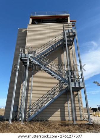 Fire Training Tower Featuring Exterior Metal Staircase And Elevated Platforms Against Clear Blue Sky, Representing Firefighter Training, Emergency Preparedness, And Safety Infrastructure