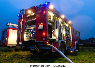 Fire truck or engine with flashing lights, lighting and hose in dusk, ready for deployment