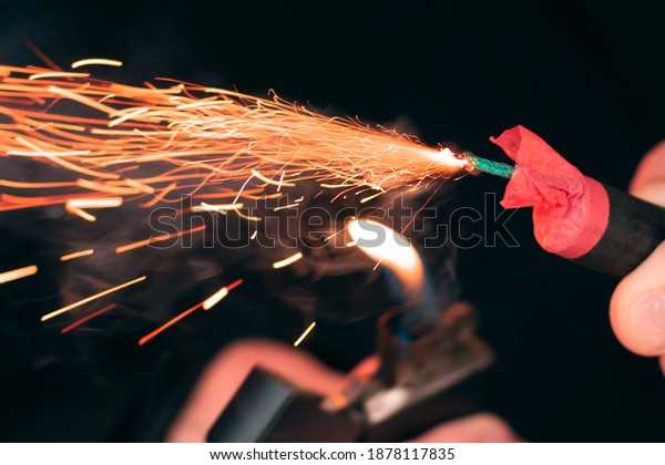 The Firecracker in a Hand. Man Holding a Burning\
Petard in His Hand. A Human with a Pyrotechnics that Burns with\
Sparks and Smoke Outdoors