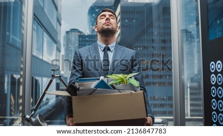 Fired Manager Going Down from Office in a Glass Elevator in Modern Business Center. Sad Specialist Laid Off in the Times of Financial Crisis and Social Turmoil, Holding Belongings in a Cardboard Box.