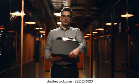 Fired Upset Man In Suit Walking Down In Office Hallway, Holding Box With Books And Personal Stuff, Saying Goodbye To Colleagues, Looking At Camera. Male Employee Leaving Marketing Company