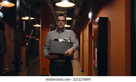 Fired Upset Man In Suit Walking Down In Office Hallway, Holding Box With Books And Personal Stuff, Saying Goodbye To Colleagues, Looking At Camera. Male Employee Leaving Marketing Company