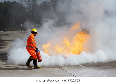 Firefighter Aim At Base Of Fire By Fire Extinguisher On Fire Conflagration With White Smoke. Occupational Health And Safety Training Concept.