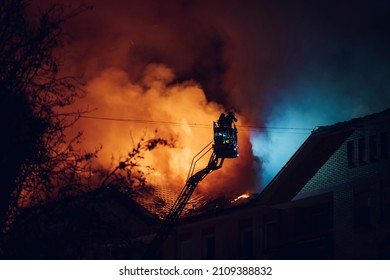 Firefighter directed hose towards the burning building at night. Boom crane with firefighters. Firefighter on pull-out crane. Firefighter extinguishes fire. - Shutterstock ID 2109388832