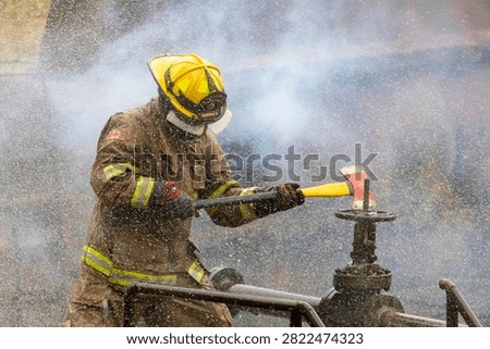 Firefighter in fireproof clothe is holding axe to destroy the water valve near burning building with high flame for fire extinguish risk rescue mission and accident management