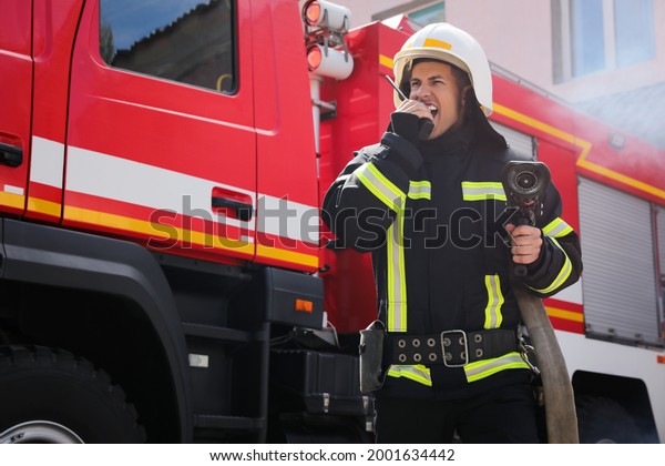 Firefighter with high pressure water jet\
using portable radio set near fire truck\
outdoors