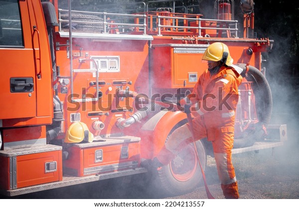 Firefighter man wearing protective fire suite\
and helmet with water car truck equipment and accessories is fire\
safety accident protection safety\
concept.