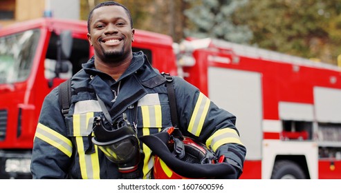 Firefighter portrait on duty. Photo of happy fireman with gas mask and helmet near fire engine