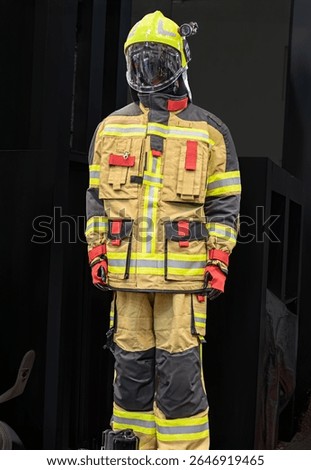 Firefighter in protective gear, standing before a barred window, daytime lighting Yellowred helmet, goggles, high-visibility jacket, black trousers with yellow stripes, gloves, tool or device on be