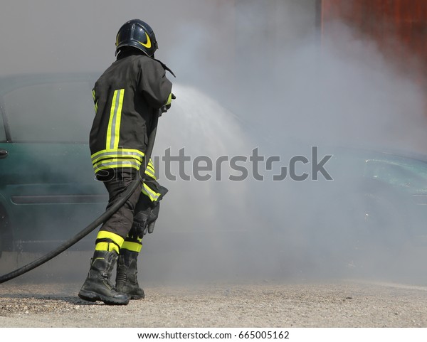 firefighter with protective\
uniform and helmet turn off the fire at the car crashed during a\
fire drill
