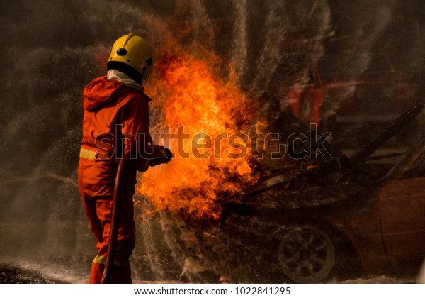 Firefighter is spraying water to extinguish the fire\
on a burning car.