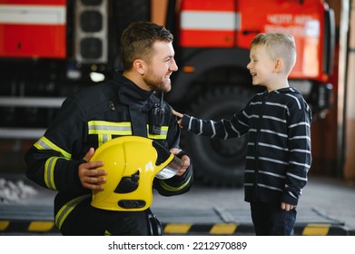 A firefighter take a little child boy to save him. Fire engine car on background. Fireman with kid in his arms. Protection concept