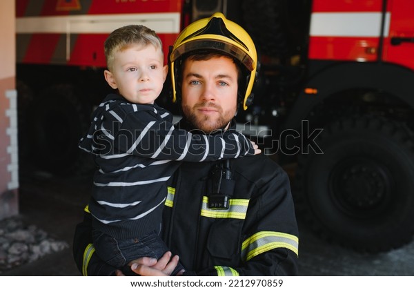 A firefighter take a little child boy to save\
him. Fire engine car on background. Fireman with kid in his arms.\
Protection concept