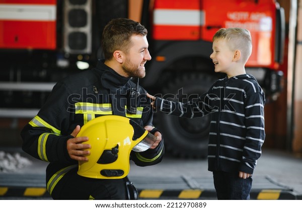 A firefighter take a little child boy to save\
him. Fire engine car on background. Fireman with kid in his arms.\
Protection concept