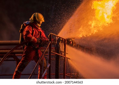 Firefighter in the training with fire hose nozzle spraying high pressure water to fire, Firefighter wearing a fire suit for safety under the danger case