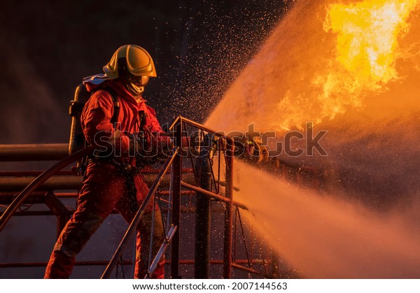 Firefighter in the training with fire hose\
nozzle spraying high pressure water to fire, Firefighter wearing a\
fire suit for safety under the danger\
case