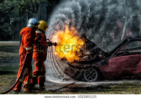 Firefighter training, Fireman annual training fire\
fighting hosing water to extinguish a fire over the accident car \
on the wayside road