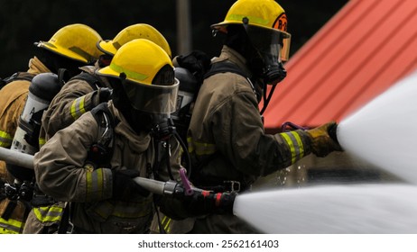 Firefighter Training. Fireman using water and extinguisher for fighting with fire flame in an emergency situation. Under danger situation all firemen wearing fire fighter gear for safety.